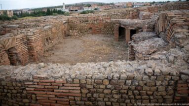 Sunken ruined room with thick stone-and-brick walls, arched brickwork, and a low rectangular opening.