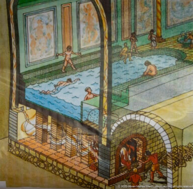 Cutaway reconstruction of Roman baths with pools above and furnace-heated underfloor spaces below.