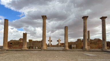 Tall surviving columns and broad stone steps among Roman ruins under a cloudy sky.