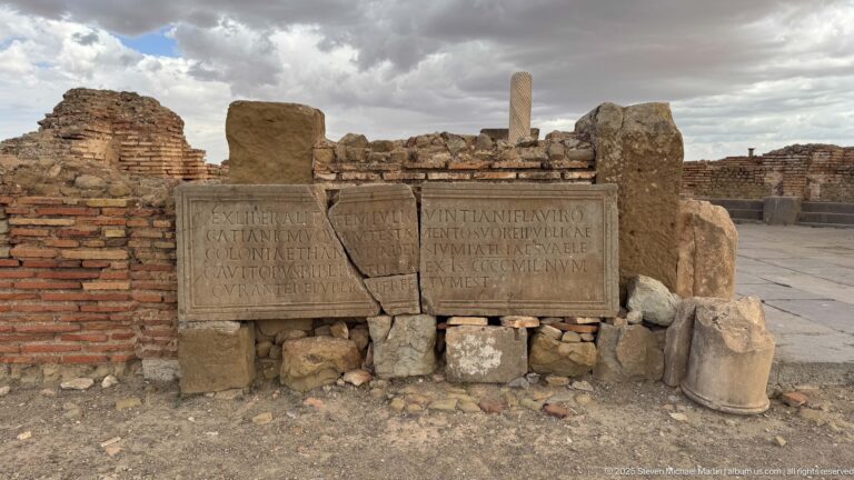 Latin-inscribed stone blocks propped against brick masonry among the ruins of Timgad.