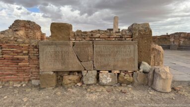 Latin-inscribed stone blocks propped against brick masonry among the ruins of Timgad.