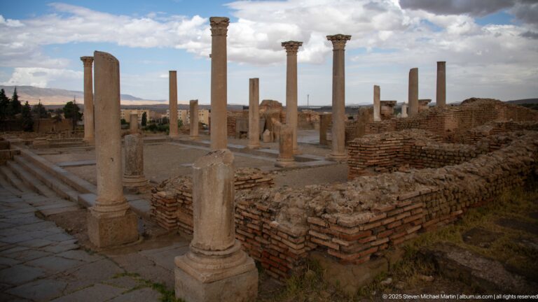 Rows of Roman columns, steps, and brick foundations forming a public architectural complex at Timgad.