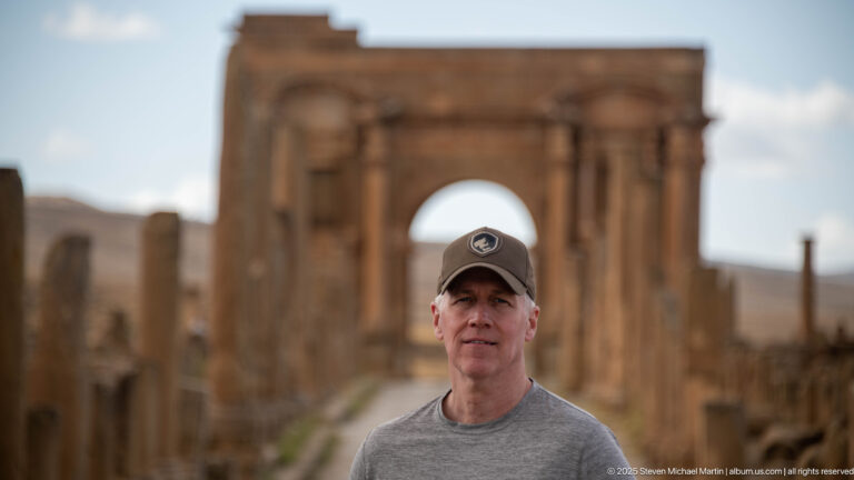 Close portrait of a visitor with the softly blurred Arch of Trajan behind him at Timgad.