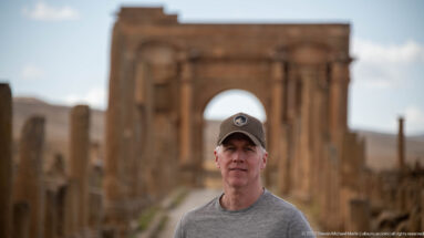 Close portrait of a visitor with the softly blurred Arch of Trajan behind him at Timgad.