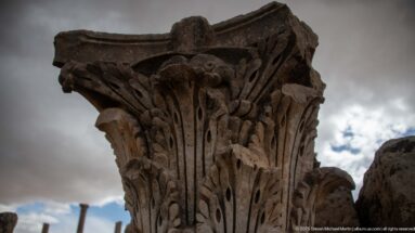 Close view of a weathered Corinthian capital carved with layered acanthus leaves against the sky.