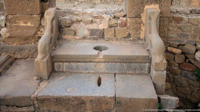 Single stone latrine seat with circular opening, frontal slot, and curved side dividers at Timgad.