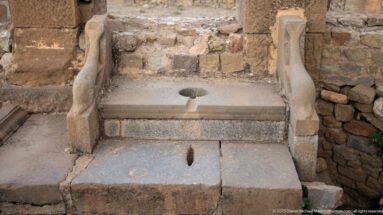 Single stone latrine seat with circular opening, frontal slot, and curved side dividers at Timgad.