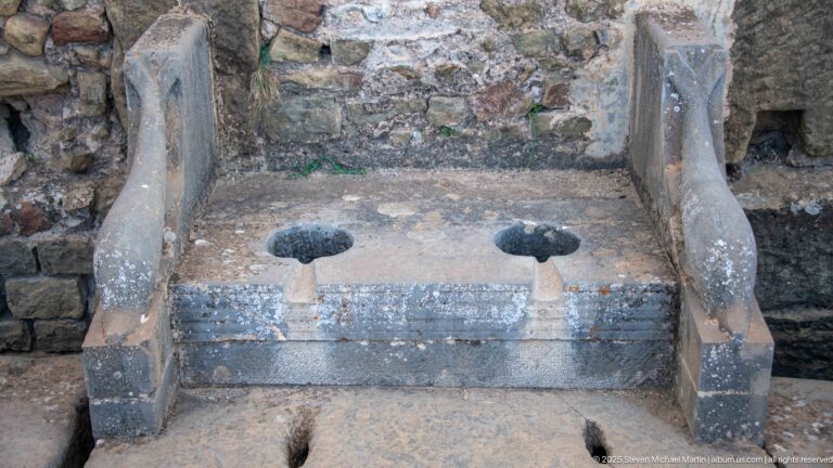 Two adjacent stone latrine openings with frontal slots and curved side partitions at Timgad.