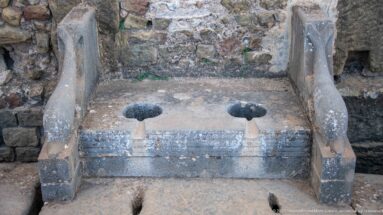 Two adjacent stone latrine openings with frontal slots and curved side partitions at Timgad.