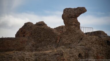 Eroded masses of Roman brick and rubble masonry rising above lower ruins at Timgad.