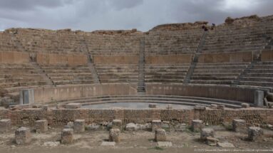 Centered view across the orchestra toward curved tiers of stone seating in Timgad’s Roman theater.