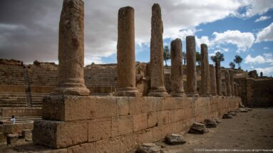 Row of tall stone columns beside the seating of Timgad’s Roman theater, with fallen blocks at ground level.