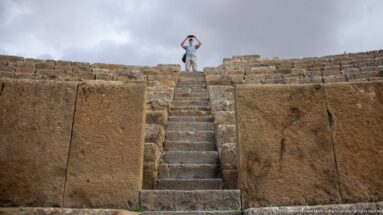 Steep stone stairway through the upper seating of Timgad’s Roman theater, with a visitor standing at the top.