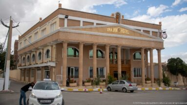 Street view of the Trajan Hotel with a columned portico, beige façade, and parked cars.
