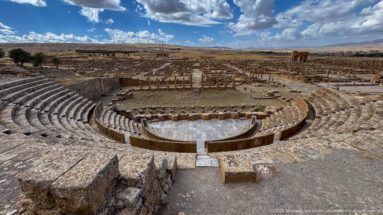 Panoramic view from Timgad’s theater over the orchestra, ruins, colonnaded city, and distant plateau.