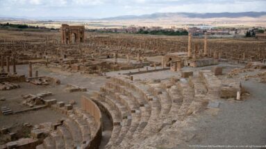 Curved theater seating in the foreground overlooking the dense archaeological remains of Timgad.