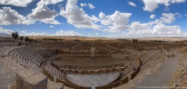 Ultra-wide view of Timgad’s Roman theater, archaeological city, open plateau, and cloud-filled sky.