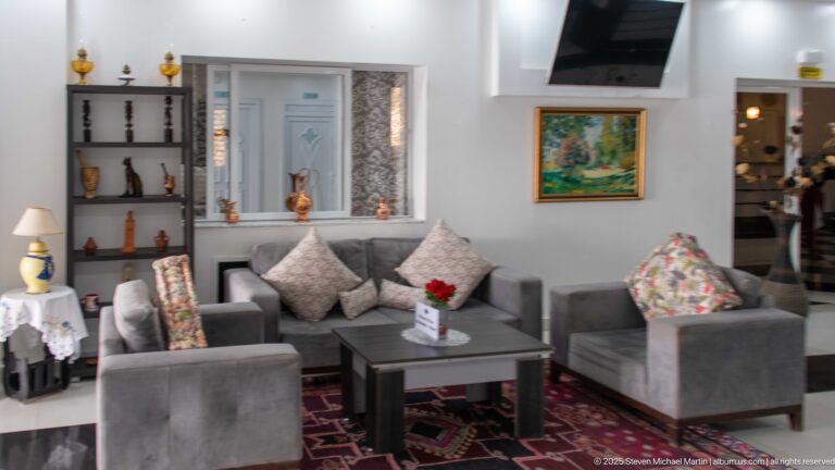 Trajan Hotel lounge with gray armchairs and sofa, patterned cushions, display niches, and framed artwork.