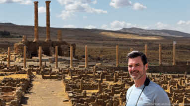Visitor in the foreground with tall Roman columns and extensive stone ruins behind at Timgad.
