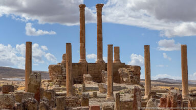 Cluster of tall Roman columns rising from substantial temple-like masonry amid the ruins of Timgad.