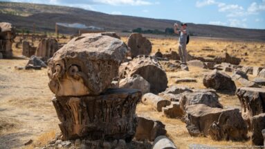 Weathered carved stone capital among fallen column drums and architectural blocks in the ruins of Timgad.