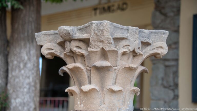 Close view of a weathered Corinthian stone capital carved with layered acanthus leaves and corner volutes.