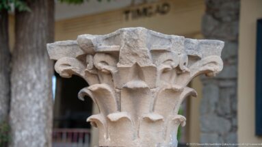 Close view of a weathered Corinthian stone capital carved with layered acanthus leaves and corner volutes.
