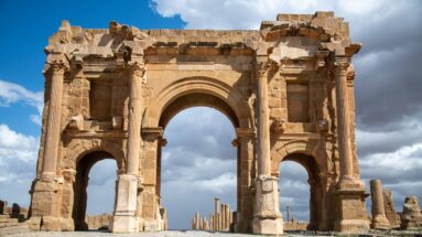 Close frontal view of the Arch of Trajan at Timgad, showing its central arch, side openings, columns, and niches.