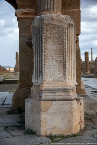 Roman stone pedestal at Timgad with a multi-line Latin inscription framed by narrow fluted decorative bands.