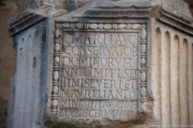 Close view of deeply carved Latin capital letters within a recessed rectangular panel on a weathered Roman stone pedestal at Timgad.