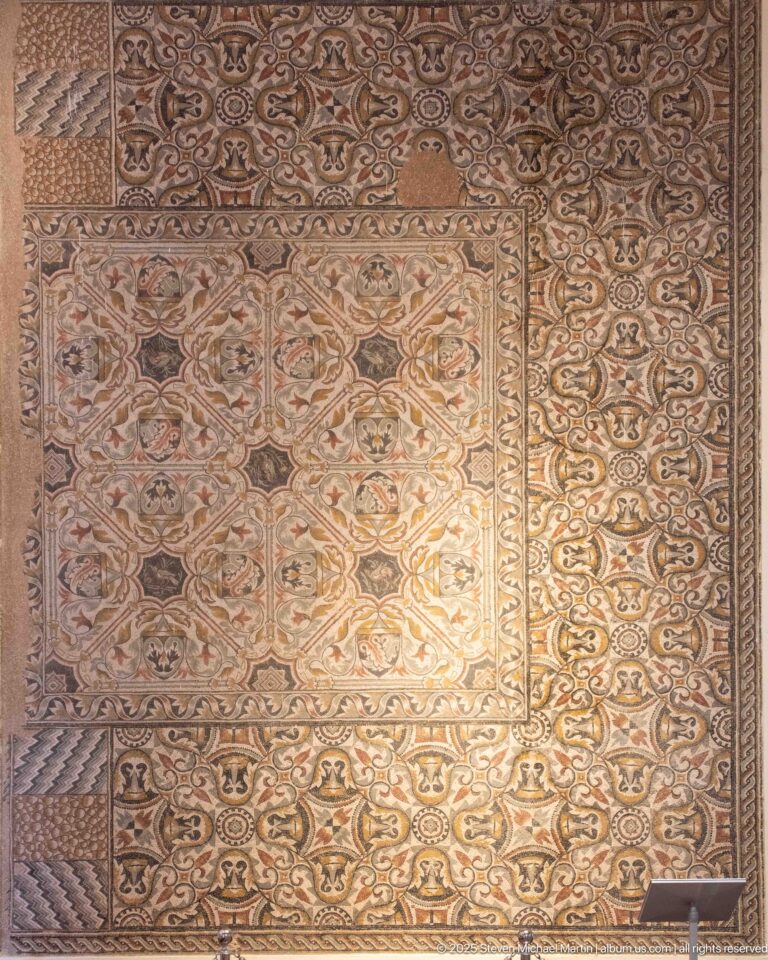 Large rectangular mosaic carpet with dense repeating floral and geometric motifs and multiple decorative borders.