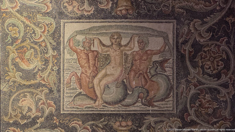 Figural Roman mosaic showing a central nude figure with two attendants, surrounded by ornate vegetal and marine motifs.