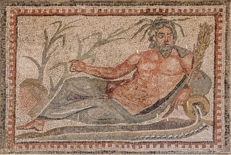 Bearded reclining male figure in a Roman mosaic, wearing red and gray drapery with vegetation and a curved form beside him.