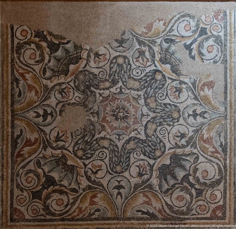 Polychrome mosaic with curling acanthus-like foliage, flowers, and small animal or bird forms woven into the design.