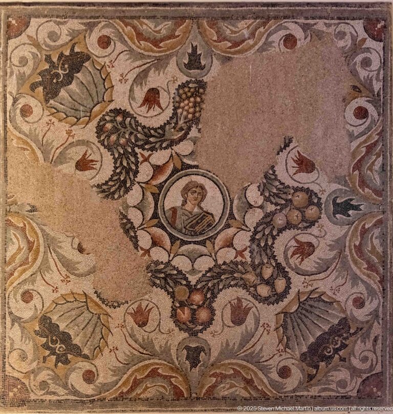 Polychrome Roman mosaic with a central human portrait medallion surrounded by birds, foliage, fruit, and scrolling ornament.