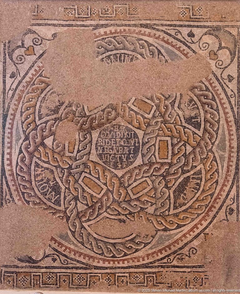 Circular Roman mosaic with a central Latin inscription surrounded by dense braided and interlaced geometric bands.