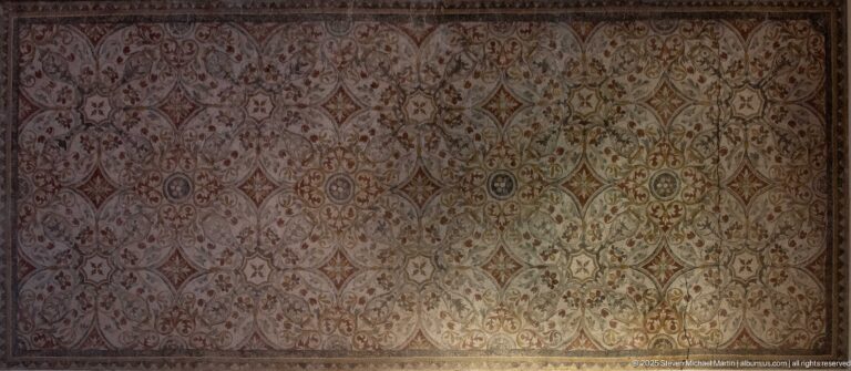 Large wall-mounted Roman mosaic with repeating elongated medallions, rosettes, and linked geometric-floral motifs.