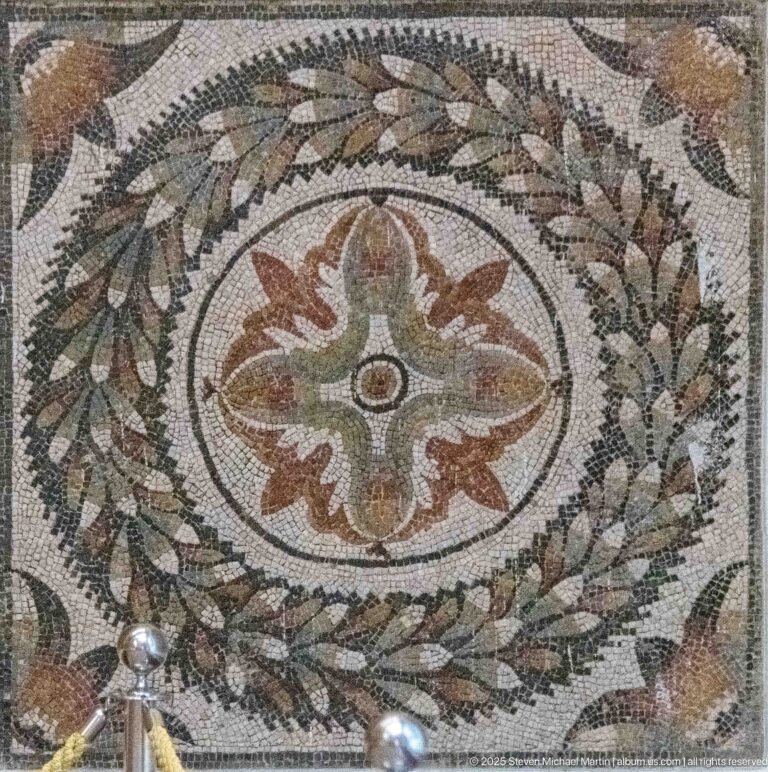 Circular Roman mosaic medallion with a four-lobed floral center surrounded by leafy and fruiting ornament.