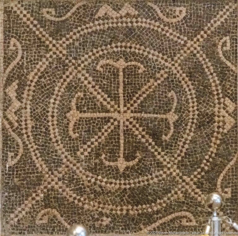 Brown-and-cream Roman mosaic with a cross-like central motif and looping geometric borders.