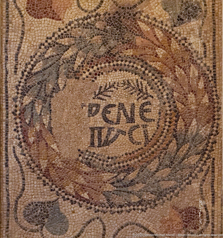Roman mosaic with a central Latin inscription surrounded by leafy and animal-like ornament.