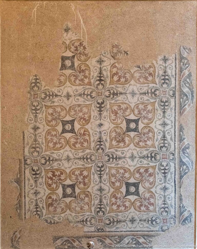 Rectangular Roman mosaic with repeating scrolling foliage and patterned borders, partly lost at the edges.