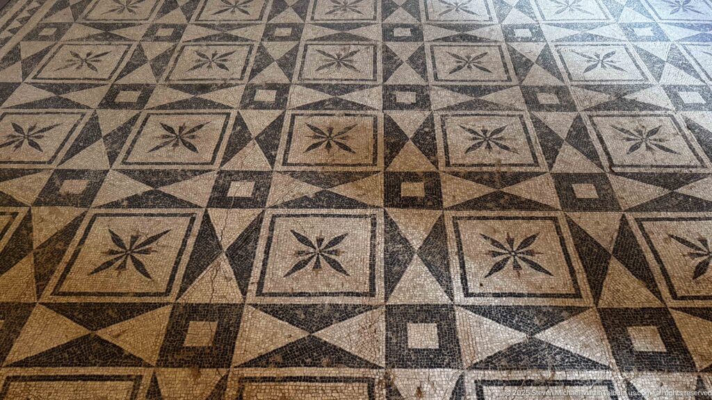 Black-and-white mosaic floor patterned with nested squares, diamonds, and repeated four-petal rosettes.