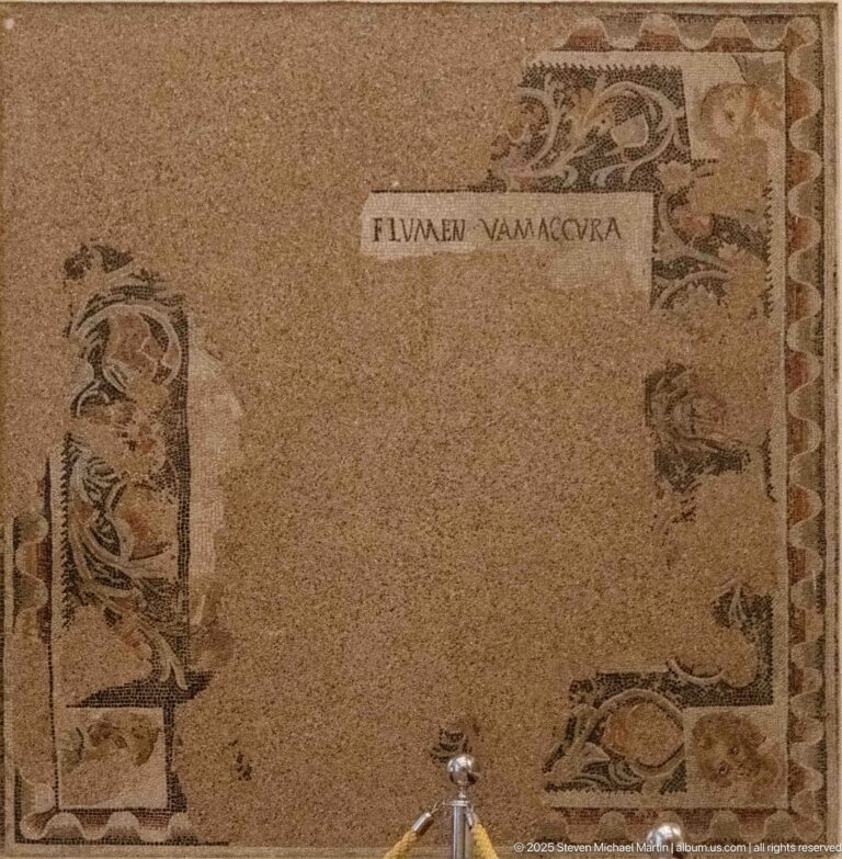 Fragmentary Roman mosaic with a Latin inscription near the top and isolated figures around the edges.