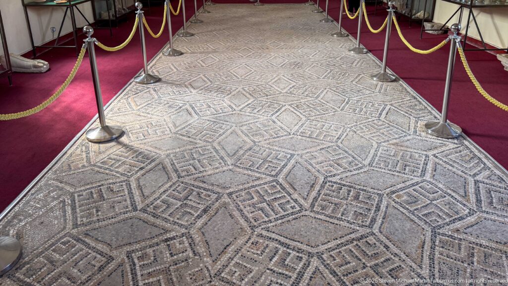 Long Roman mosaic pavement with nested diamonds and meander patterns displayed behind museum ropes.