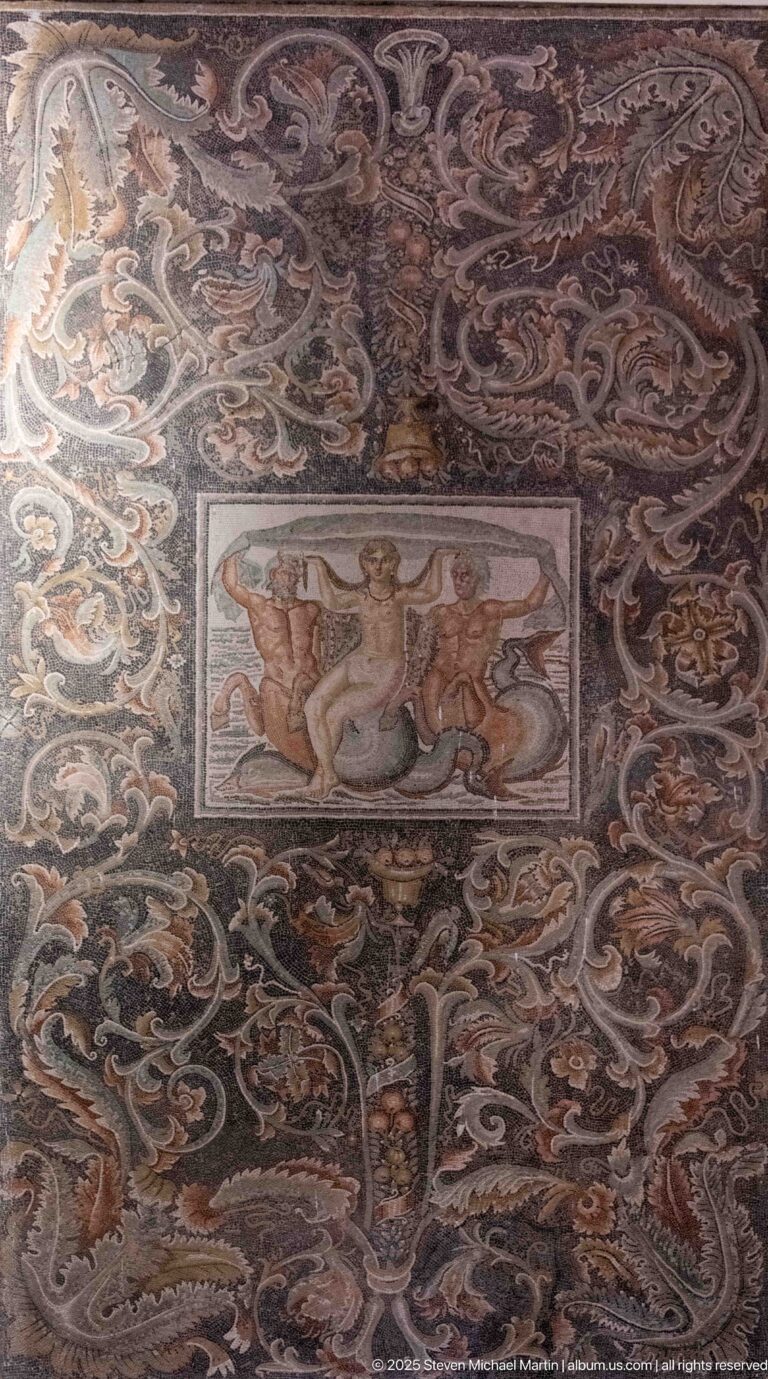 Roman mosaic with a small central marine figure framed by dense multicolored scrolling foliage.