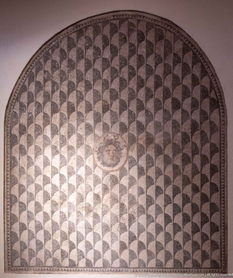 Semicircular Roman mosaic with repeating dark fan-shaped motifs and a small central circular medallion.