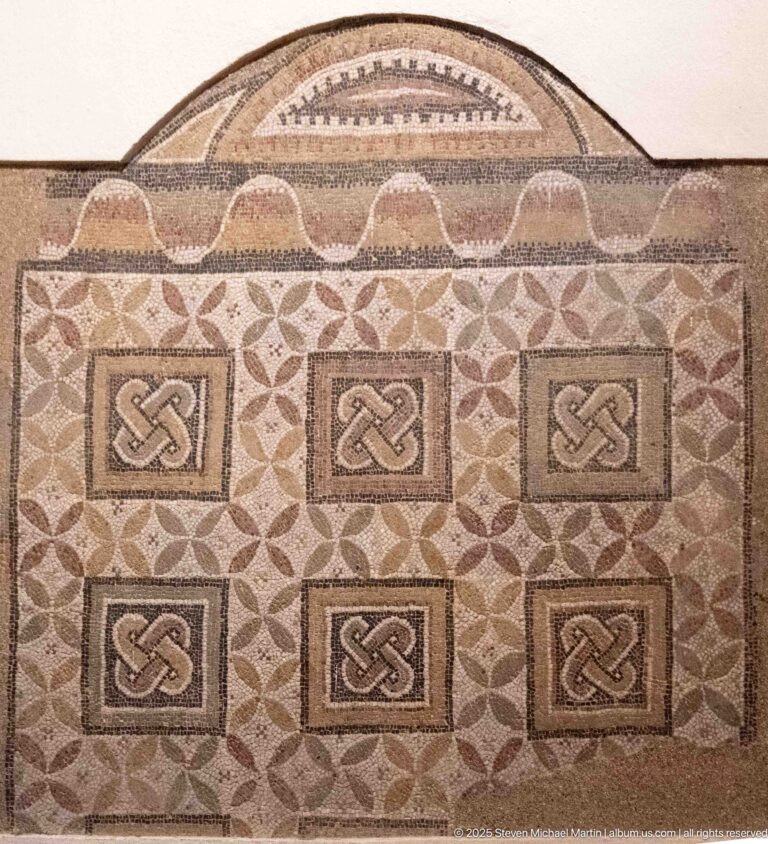 Roman mosaic with six square interlace-knot panels, repeating leaf motifs, patterned borders, and a semicircular top.