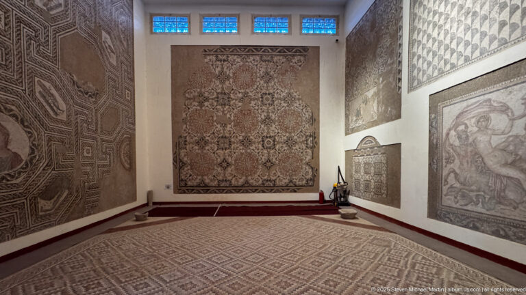 Museum corner with a geometric mosaic floor and several large Roman mosaics mounted on adjoining walls.