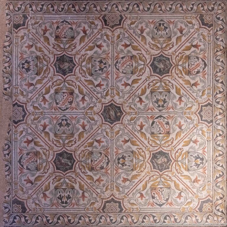 Roman mosaic with scrolling vines, stylized leaves, birds, and small animal motifs in a symmetrical polychrome design.