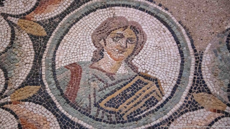 Roman mosaic portrait bust of a youthful figure inside a circular medallion with draped clothing and carefully shaded facial features.